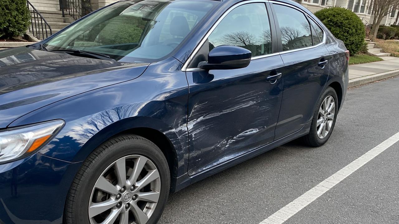 Dunkelblaue Limousine mit Kratzern und Dellen an der Fahrertür am Straßenrand